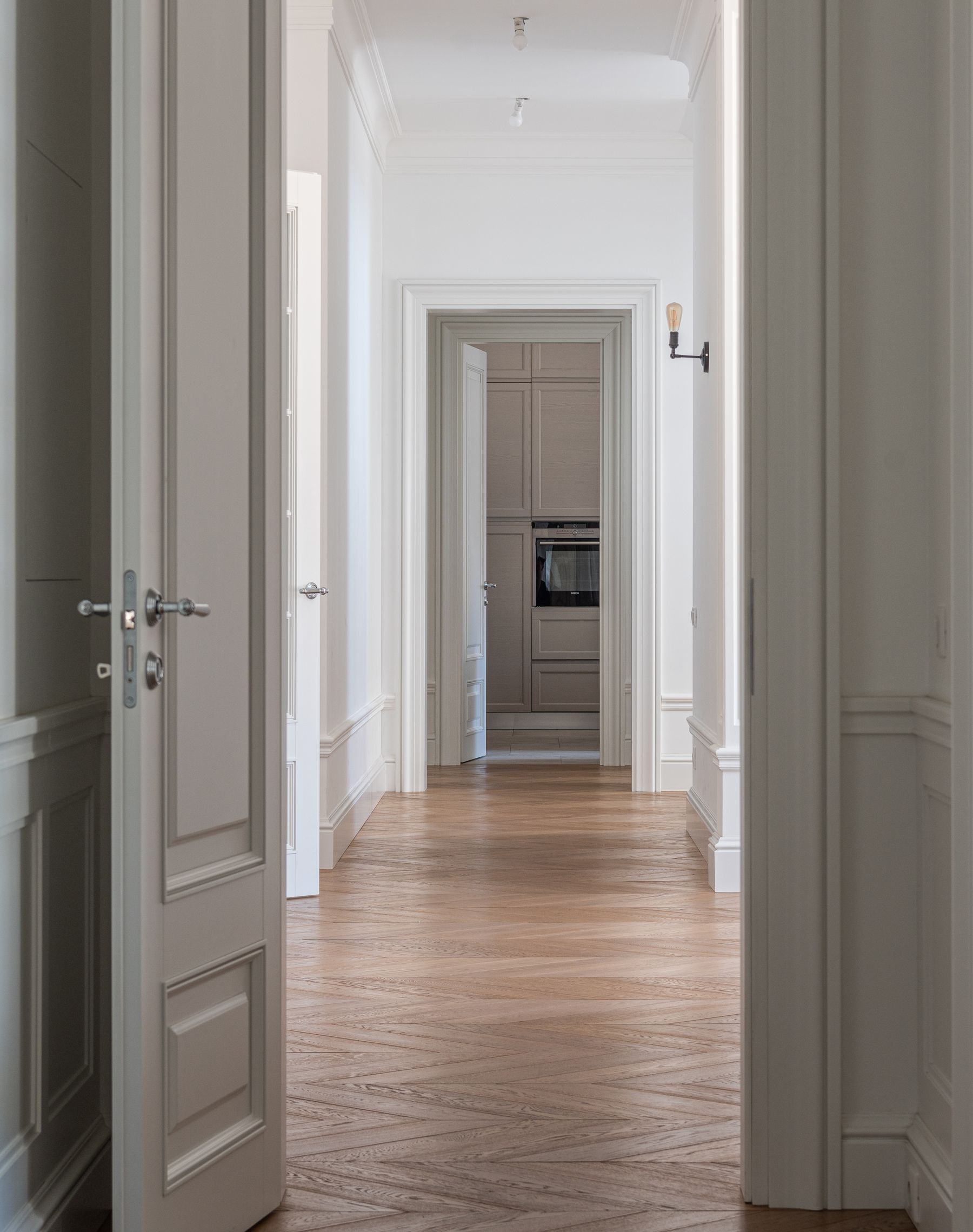 A hallway with freshly painted white walls, wainscoting and a herringbone wood floor