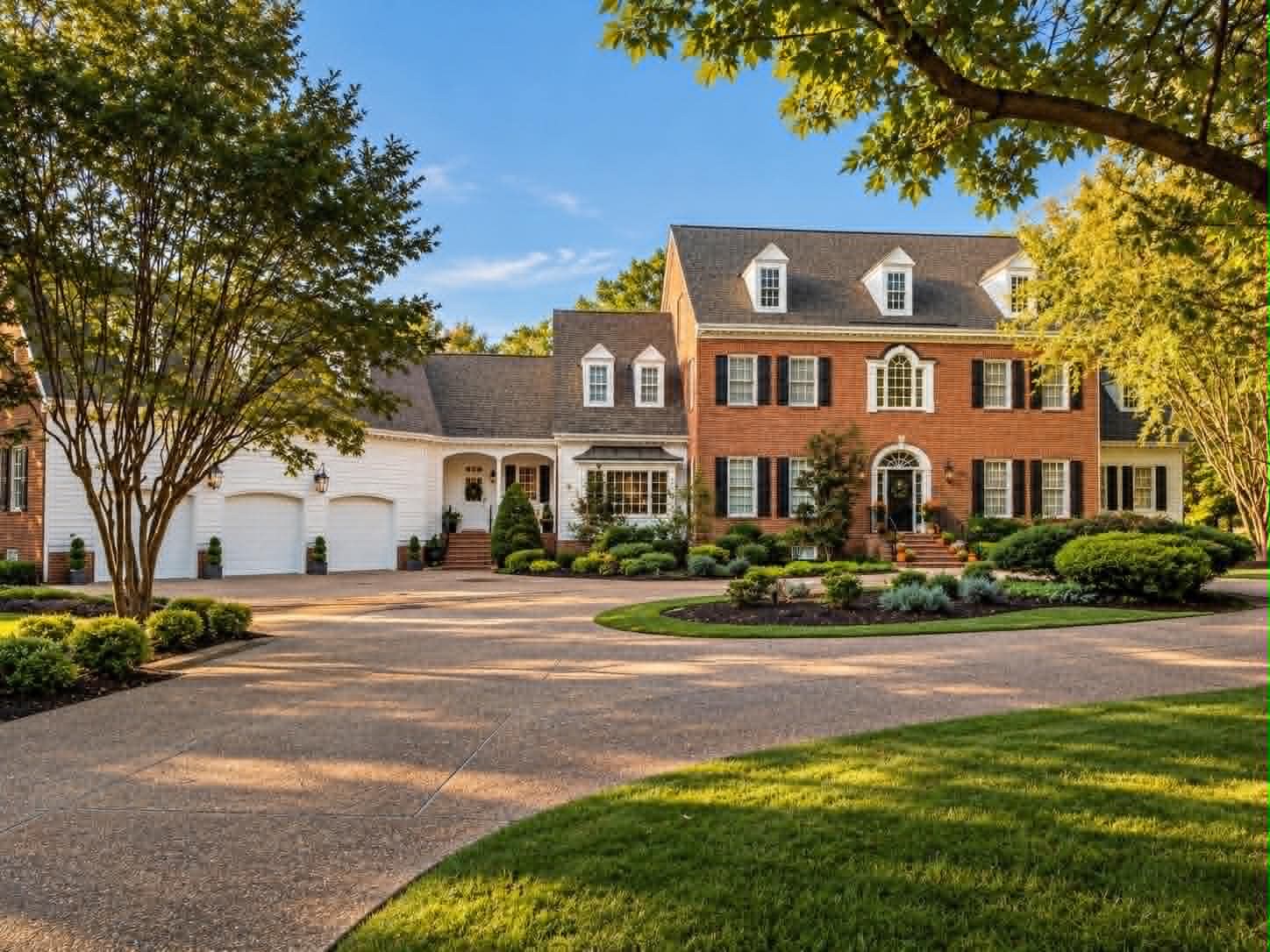 A large red brick house with bright white horizontal siding, white dormer windows and black shutters, a circular paved drive and mature shrubs and trees in front